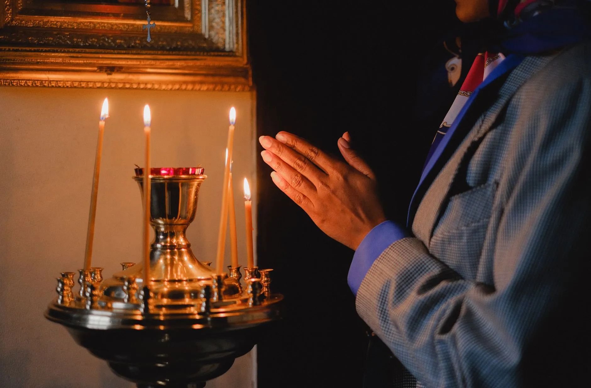 Złożone dłonie przy zapalonych świecach w religijnym wnętrzu