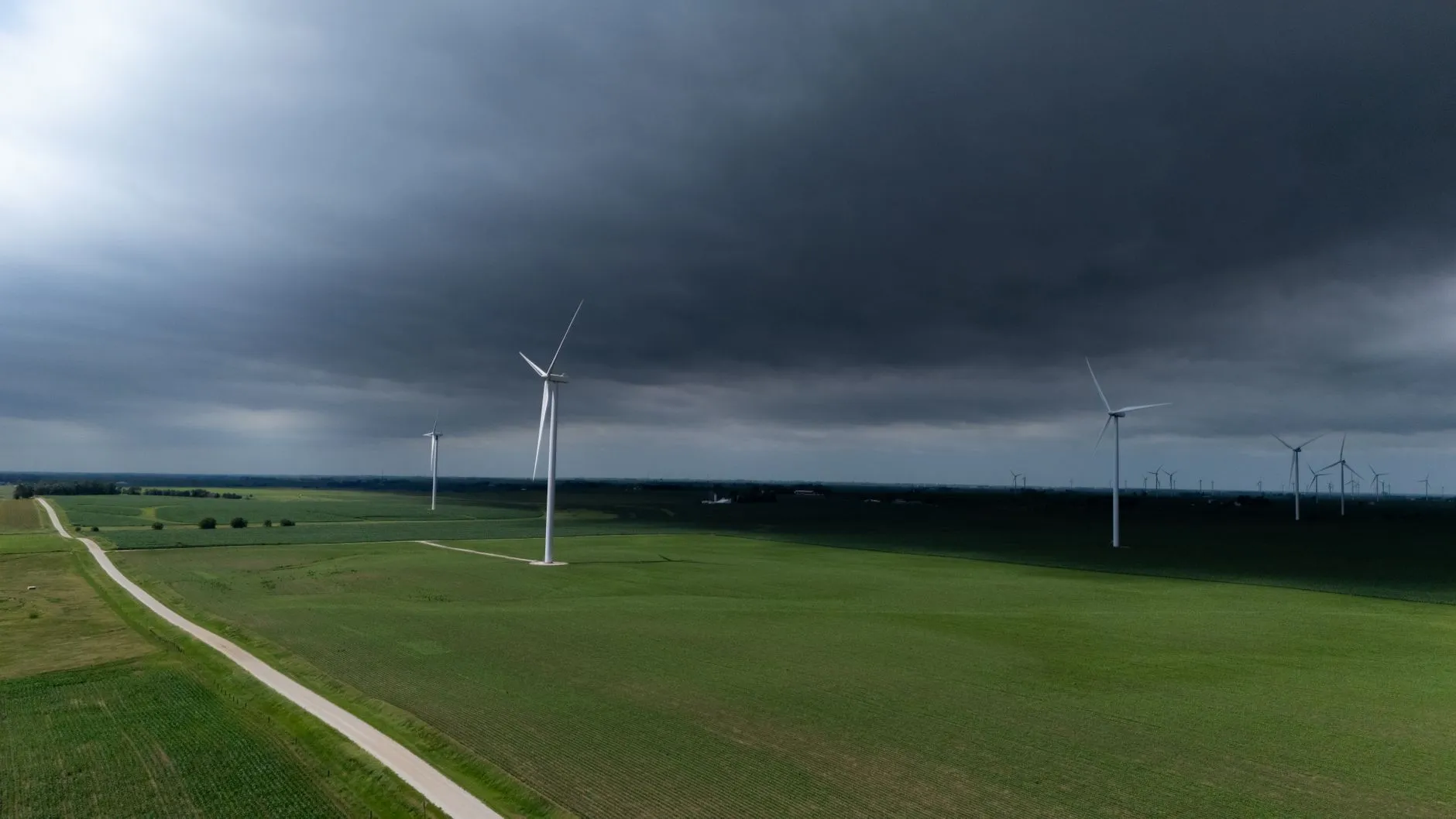 Turbiny wiatrowe na zielonych polach pod ciemnymi chmurami