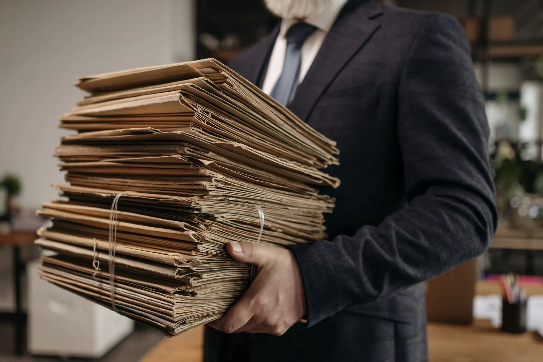 Osoba w garniturze trzymająca duży stos papierowych teczek