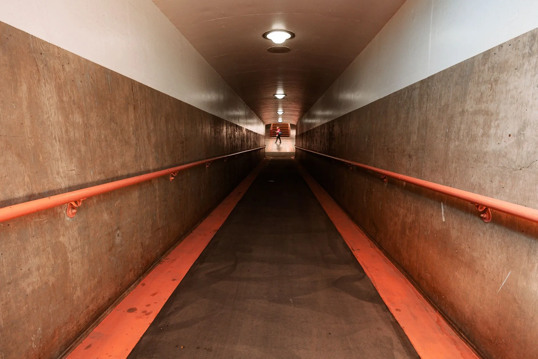Betonowy tunel z pomarańczowymi poręczami i osobą w oddali